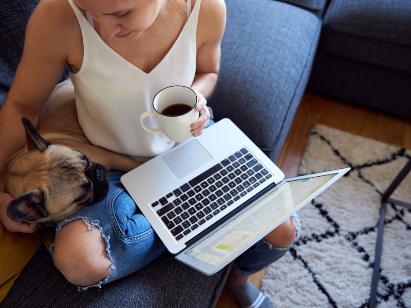 Photo: A woman pets her dog as she sits with her computer in her lap.