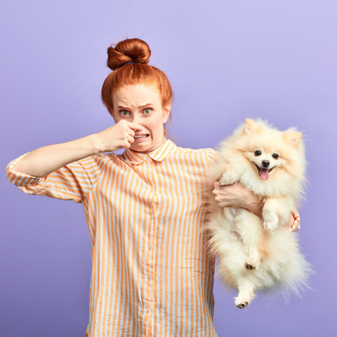 Photo of a woman holding a dog in one arm and her nose with her other hand.